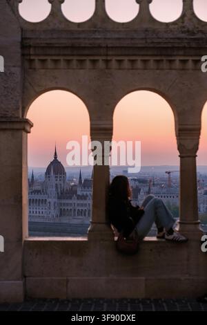 Budapest, Hongrie offre un arrière-plan de coucher de soleil à couper le souffle à la Bastion des pêcheurs, où un voyageur savoure la vue. Banque D'Images