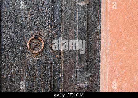 Gros plan d'une vieille porte en bois sombre avec un anneau métallique rouillé et un mur en terre cuite Banque D'Images