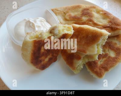 Tarte frite cassée montrant une garniture chaude de pommes de terre et de champignons porcini, servie avec de la crème fraîche, photo de stock en gros plan Banque D'Images