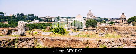La vue montre des bâtiments du Vatican depuis le Forum romain. Les gens visitent le site pendant la journée. Le soleil brille sur les ruines anciennes et la ligne d'horizon de la ville. Banque D'Images