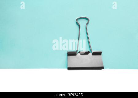 Pince à reliure sur une feuille de papier bleu clair vierge isolée sur fond blanc Banque D'Images