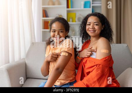 Mère et fille noires souriantes montrant toutes deux des bras bandés après la vaccination Banque D'Images