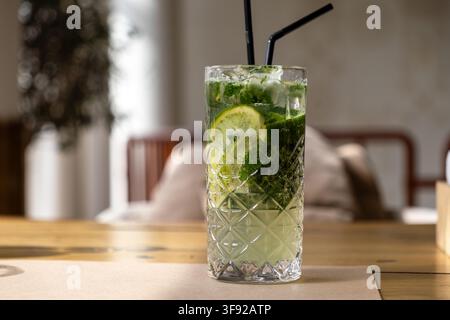 Le mojito refroidi dans un verre highball texturé contient de la glace, des agrumes et des herbes, créant une atmosphère invitante pour un repas social ou une célébration Banque D'Images