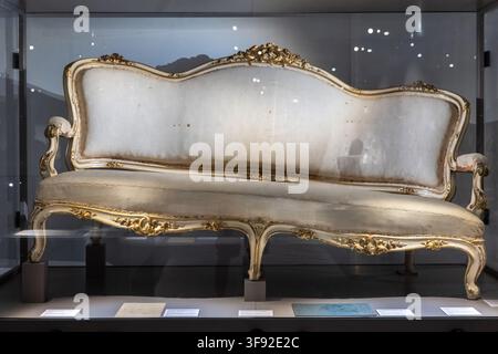 VIENNE, AUTRICHE, 13 août 2026 : Un canapé capitonné antique orné de détails sculptés dorés est exposé derrière une vitre dans une vitrine de musée. Banque D'Images