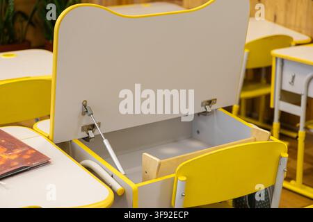 Bureau d'école jaune moderne et vide avec un couvercle ouvert dans une classe d'élémentaire, créant une atmosphère lumineuse pour que les enfants étudient et rangent leurs fournitures scolaires Banque D'Images