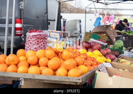 Des oranges mûres et brillantes disposées en tas sur un étal de marché avec des grenades et des radis en arrière-plan, promouvant le commerce agricole biologique et Banque D'Images