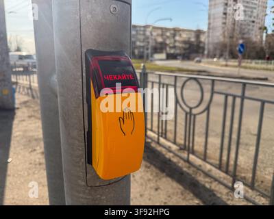 Kiev, Ukraine - 20 mars 2026 : Bouton poussoir jaune pour piétons à un poteau de feu tricolore sur une rue de la ville, affichant un signal d'attente pour garantir une sécurité c Banque D'Images