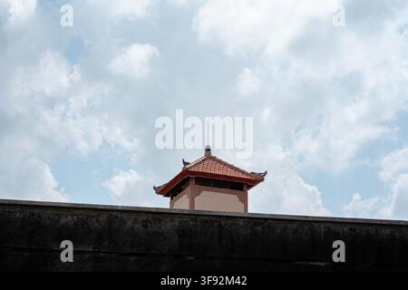 Prise de vue en contre-plongée d'un toit de tour décoratif avec un clocheton au sommet d'un mur érodé, sur fond de ciel nuageux. Banque D'Images