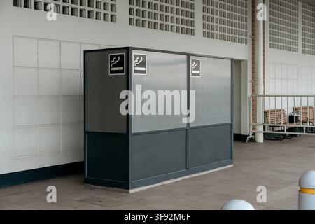 Abri moderne désigné pour fumer en extérieur avec cadre en métal sombre, panneaux translucides et panneaux de symboles de fumeur à l'extérieur d'un bâtiment. Banque D'Images