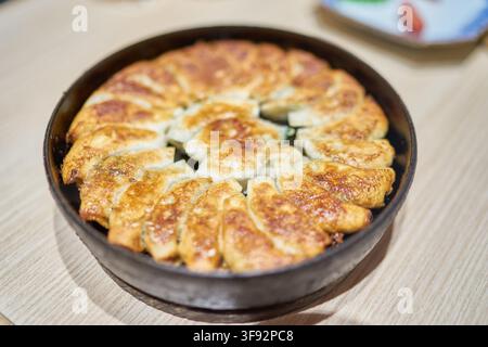 Des gyoza japonais croustillants frits servis dans une poêle ronde sur une table en bois. Banque D'Images