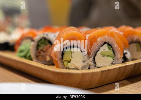 Pièces de sushi appétissantes mettant en vedette du poisson cru, du fromage crémeux et de l'avocat croustillant, servies sur une planche rustique, représentant une cuisine japonaise savoureuse Banque D'Images