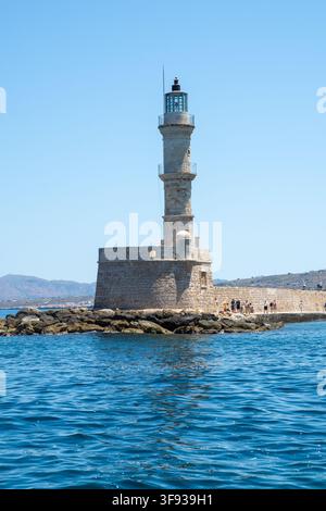 Vue du phare historique de Chania dressé sur le quai en pierre de la marina de la vieille ville avec des gens qui marchent à proximité sous un ciel bleu clair à Chania Banque D'Images