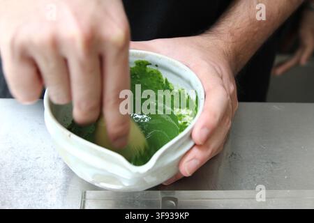 Cliché en gros plan d'une action de fouettage d'un thé matcha vert dans un bol blanc avec un fouet en bambou. Banque D'Images