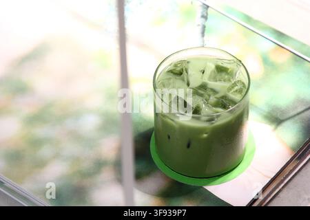 Un verre rafraîchissant de matcha latte glacé avec des glaçons posé sur un dessous de verre vert assorti sur une surface de table minimaliste. Banque D'Images