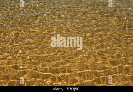 Eau de mer cristalline scintillant au soleil et ondulant doucement sur une plage de sable doré isolée. Côte de l'Alentejo, Portugal. Banque D'Images