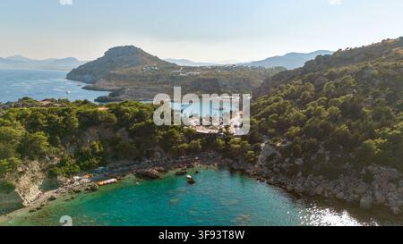 Une forêt de pins couvre les pentes de la vallée qui descendent vers une crique turquoise ouverte sur la mer brumeuse, Rhodes, Grèce. Banque D'Images