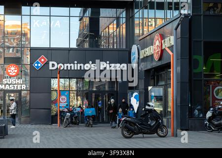 Kiev, Ukraine - 15 mars 2026 : Entrée d'un point de vente Domino's Pizza située dans un bâtiment commercial moderne en verre à côté d'un restaurant Puzata Hata, montrant Banque D'Images