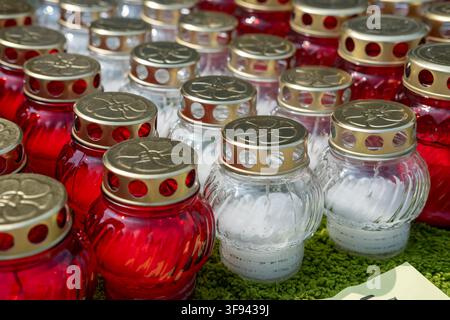 Des bougies funéraires rouges et blanches dans des bocaux en verre sont regroupées sur la table d'un vendeur de marché. Banque D'Images