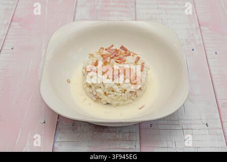 Risotto carbonara moulé avec des morceaux de jambon servi dans un bol blanc sur une table en bois rose usée. Banque D'Images