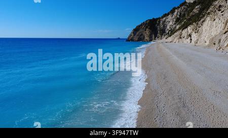 Une plage déserte époustouflante avec une eau turquoise vibrante et des falaises de calcaire dramatiques sous un ciel bleu clair. Des vagues douces se brisent sur le rivage de sable blanc dans Banque D'Images