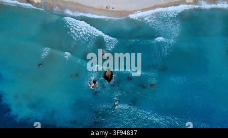 Photographie aérienne époustouflante capturée par drone montrant des vagues turquoise de l'océan s'écrasant sur une plage de sable, avec des rochers submergés visibles à travers une eau cristalline Banque D'Images