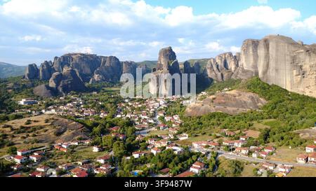 Vue aérienne des impressionnants piliers rocheux des Météores dominant un village grec pittoresque niché parmi des collines verdoyantes. Banque D'Images