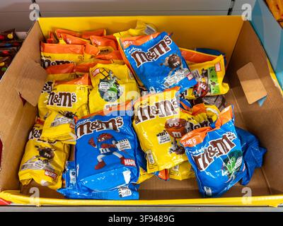 Italie - 14 août 2026 : boîte de présentation en carton remplie d'un assortiment de sachets jaunes et bleus de bonbons au chocolat croquants M&M dans une épicerie Banque D'Images