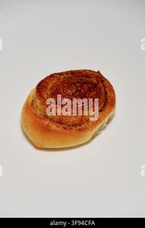 Photographie rapprochée commerciale d'un délicieux roulé à la cannelle doré et fraîchement cuit, présentant une texture en spirale attrayante, isolé sur une surface blanche propre. Banque D'Images