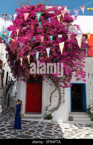 Bougainvilléa sur une porte rouge avec des fanions colorés dans une ruelle blanchies à la chaux, Mykonos, Grèce. Banque D'Images