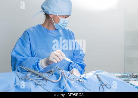 Une chirurgienne est concentrée sur sa tâche dans un hôpital. Elle travaille sur un patient entourée d'outils chirurgicaux. Banque D'Images