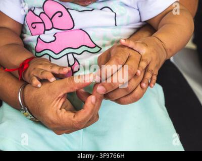 Photographie en gros plan d'un bébé entouré de mains adultes attentionnées, capturant un moment tendre de connexion et d'affection familiale. L'image se concentre sur tou Banque D'Images