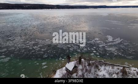 Vue aérienne du phare de Grand Island entouré d'arbres enneigés et des eaux gelées du lac Supérieur à Munising, Michigan, États-Unis. Banque D'Images