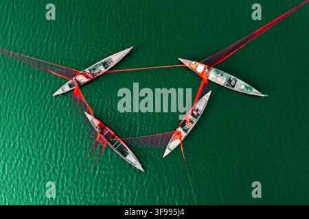 Vue aérienne de quatre bateaux de pêche en bois reliés par des filets rouges sur l'eau verte d'une rivière à Bogura, division de Rajshahi, Bangladesh, avec des pêcheurs au travail. Banque D'Images