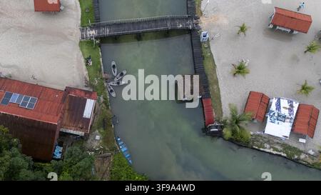 Vue aérienne de la plage de McCarthy présentant une entrée de rivière, une passerelle en bois, de petites embarcations amarrées le long de la berge et des cabanes aux toits rouges sur le sable Banque D'Images