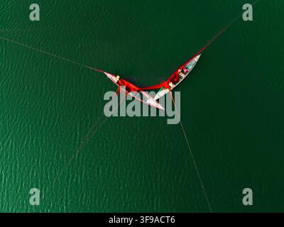 Vue aérienne de deux petits bateaux tirant un grand filet de pêche rouge à travers le fleuve vert et calme à Bogura, division de Rajshahi, Bangladesh. Banque D'Images
