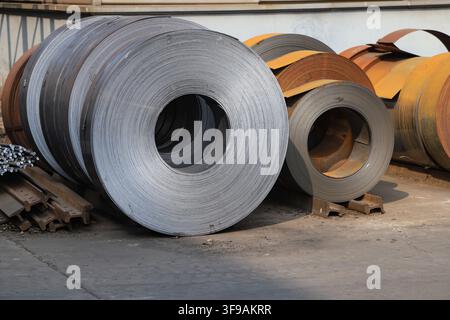 L'image capture des bobines d'acier laminées à chaud soigneusement empilées dans un environnement de stockage industriel. Les surfaces métalliques présentent une teinte gris argenté fraîche avec Banque D'Images