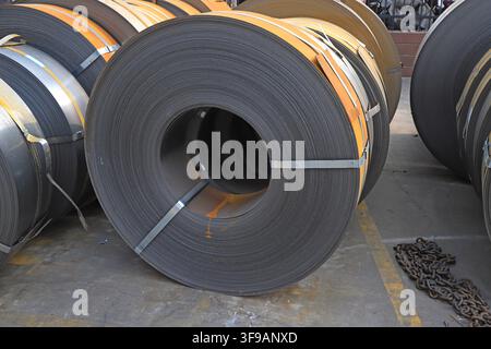 L'image capture des bobines d'acier laminées à chaud soigneusement empilées dans un environnement de stockage industriel. Les surfaces métalliques présentent une teinte gris argenté fraîche avec Banque D'Images