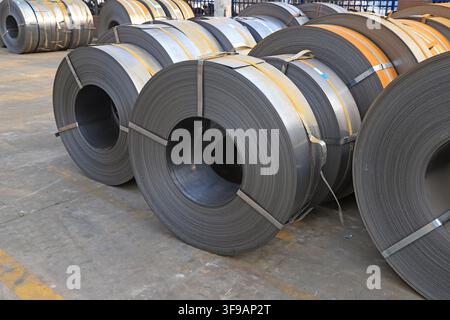 L'image capture des bobines d'acier laminées à chaud soigneusement empilées dans un environnement de stockage industriel. Les surfaces métalliques présentent une teinte gris argenté fraîche avec Banque D'Images