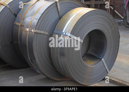L'image capture des bobines d'acier laminées à chaud soigneusement empilées dans un environnement de stockage industriel. Les surfaces métalliques présentent une teinte gris argenté fraîche avec Banque D'Images