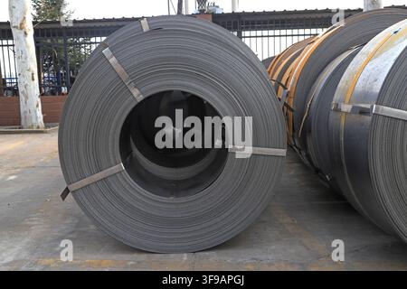 L'image capture des bobines d'acier laminées à chaud soigneusement empilées dans un environnement de stockage industriel. Les surfaces métalliques présentent une teinte gris argenté fraîche avec Banque D'Images