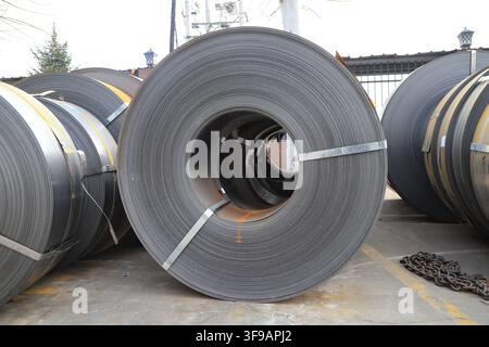 L'image capture des bobines d'acier laminées à chaud soigneusement empilées dans un environnement de stockage industriel. Les surfaces métalliques présentent une teinte gris argenté fraîche avec Banque D'Images