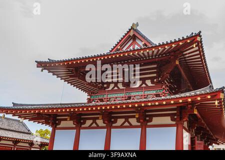 Une vue rapprochée du toit en tuiles traditionnel et des poutres en bois rouges de la porte historique Chumon du temple Shitennoji à Osaka, Japon Banque D'Images