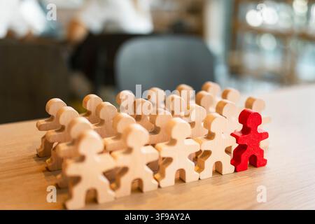 Concept de leadership démarquant avec une figure en bois rouge unique debout parmi une foule de figurines en bois neutres sur un bureau pour la gestion d'entreprise. Banque D'Images