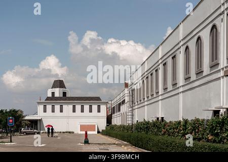 Une photographie extérieure en grand angle en journée d'un grand bâtiment industriel ou commercial blanc présentant des fenêtres à volets cintrées classiques, une tour soignée. Banque D'Images