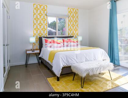 Une location de vacances pour chambre moderne, lumineuse et colorée, avec un papier peint géométrique, un tapis jaune et une literie vibrante. Banque D'Images
