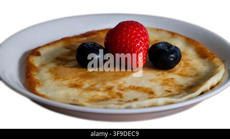 Fine crêpe garnie de fraises rouges fraîches et de myrtilles sur une assiette blanche isolée Banque D'Images