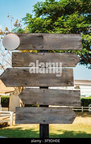 Panneaux flèches en bois vierges rustiques empilés sur un poteau en plein air dans un jardin ensoleillé avec des arbres verts et un ciel bleu Banque D'Images