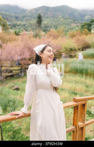 Portrait joyeux d'une touriste en robe blanche profitant d'un pont en bois sous des cerisiers himalayens sauvages en fleurs pendant le printemps à Khun Wang, Chia Banque D'Images