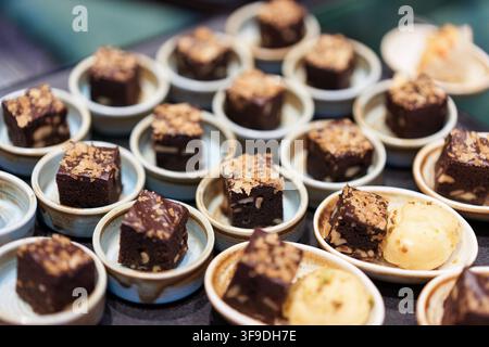 Brownies au chocolat noir riches garnis de noix et de miettes, servis dans de petites coupelles en céramique comme des portions de dessert élégantes lors d'un buffet d'événement de traiteur Banque D'Images