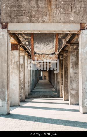 Des colonnes en béton érodées et des poutres en acier rouillées forment un couloir répétitif dans une structure industrielle abandonnée, créant une forte perspective en point de fuite Banque D'Images